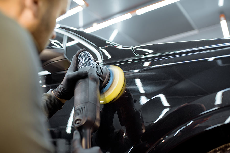 A car detailing professional in Springfield, IL using a tool to wax the exterior of a black vehicle and remove scratches.