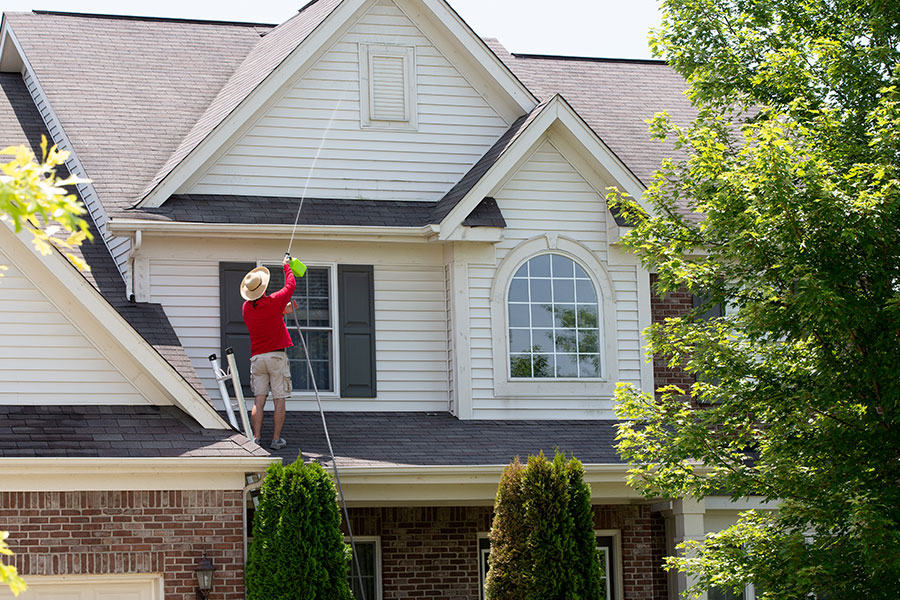 A power washing professional in a red shirt using a power washing device to clean the white siding of a home in Springfield, IL.
