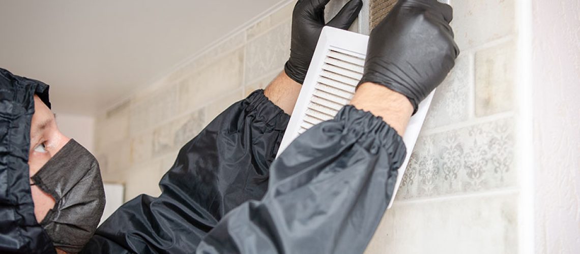 A professional air duct cleaning technician in a black suit, black mask, and gloves, cleaning the inside of an air duct system in Springfield, IL