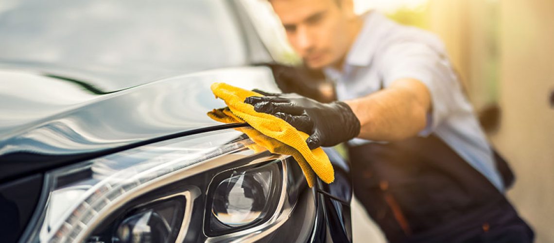 A car detailing expert in Springfield, IL using a yellow rag to clean and detail the exterior of a vehicle for a client.